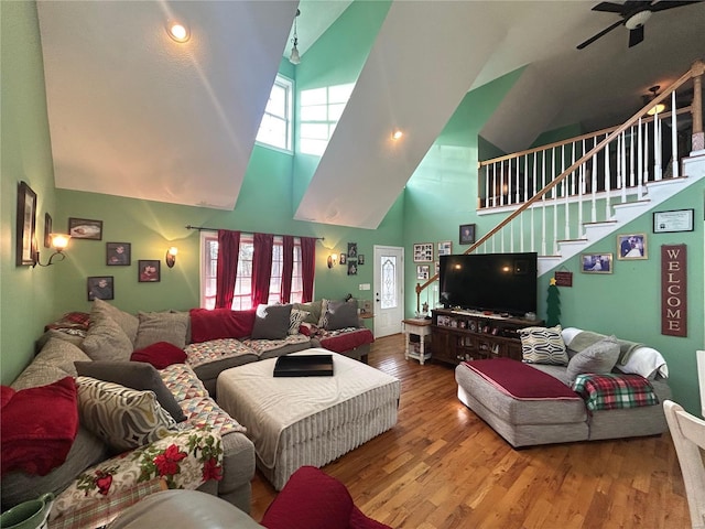 living area with a high ceiling, stairs, ceiling fan, and wood finished floors