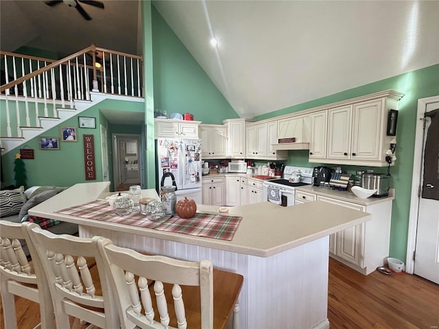 kitchen featuring light wood finished floors, a breakfast bar area, light countertops, white appliances, and high vaulted ceiling
