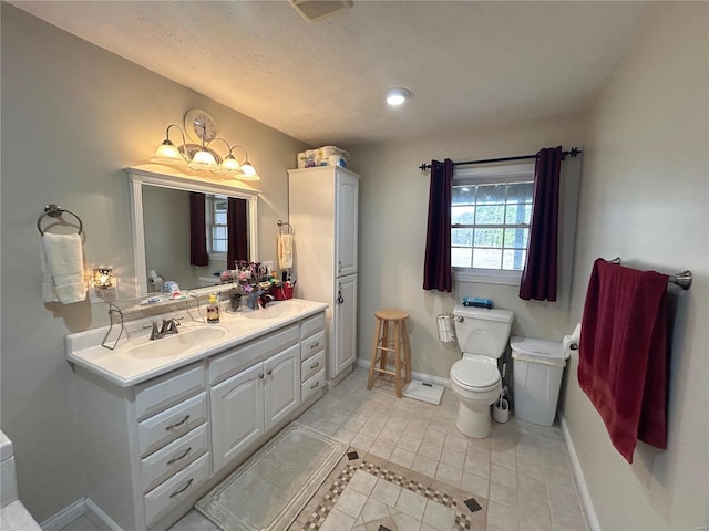 bathroom with baseboards, double vanity, a sink, tile patterned flooring, and toilet