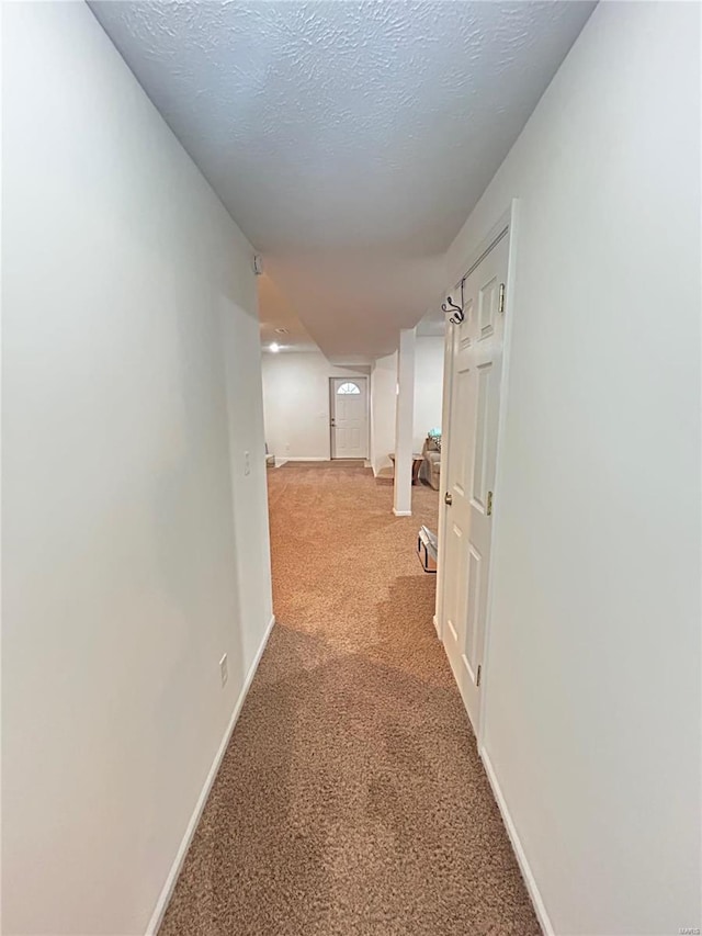 hallway featuring light colored carpet, baseboards, and a textured ceiling