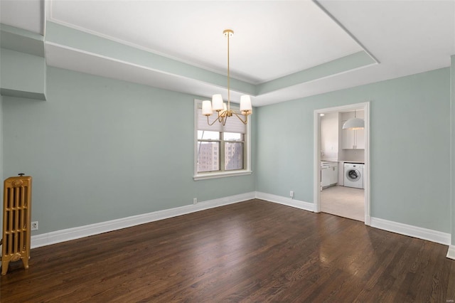 unfurnished room with a notable chandelier, washing machine and dryer, a raised ceiling, dark wood-style floors, and baseboards