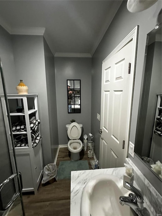 bathroom featuring toilet, ornamental molding, a sink, wood finished floors, and baseboards