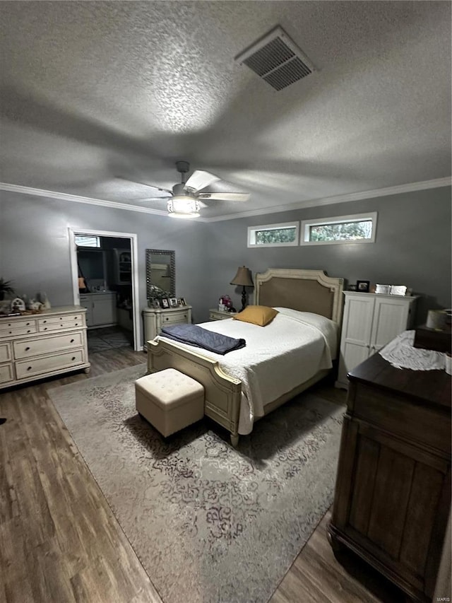 bedroom featuring dark wood finished floors, visible vents, a textured ceiling, and crown molding
