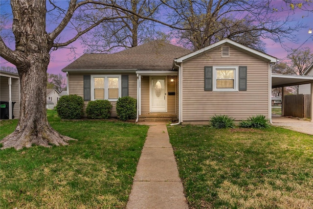 bungalow-style house with a yard, a shingled roof, fence, driveway, and an attached carport