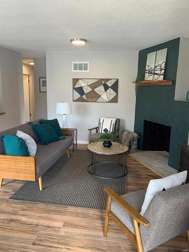 living room featuring visible vents, a fireplace, a textured ceiling, and wood finished floors