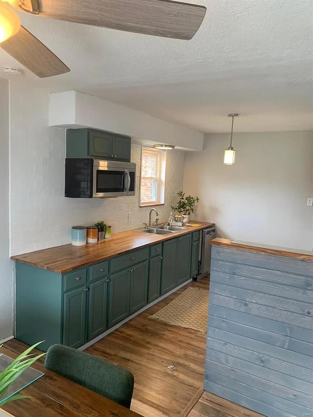 kitchen with dark wood-type flooring, a sink, appliances with stainless steel finishes, green cabinets, and wooden counters