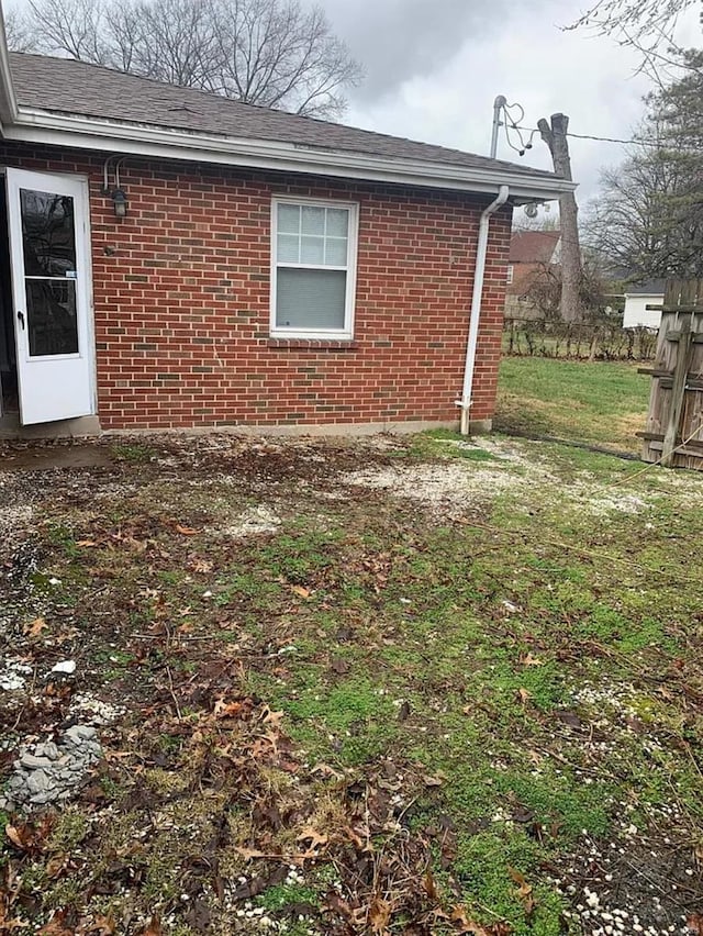 view of side of property with brick siding, a lawn, and a shingled roof