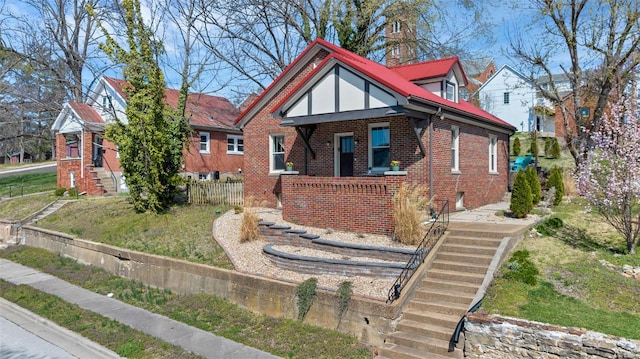 tudor house with a front yard, covered porch, fence, and brick siding