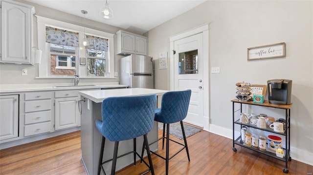 kitchen with light countertops, a sink, freestanding refrigerator, wood finished floors, and a kitchen breakfast bar