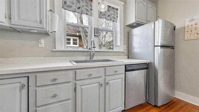 kitchen featuring light countertops, baseboards, a sink, dark wood-style floors, and appliances with stainless steel finishes