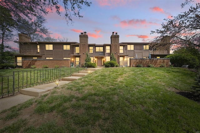 back of property at dusk featuring fence, a lawn, and a chimney