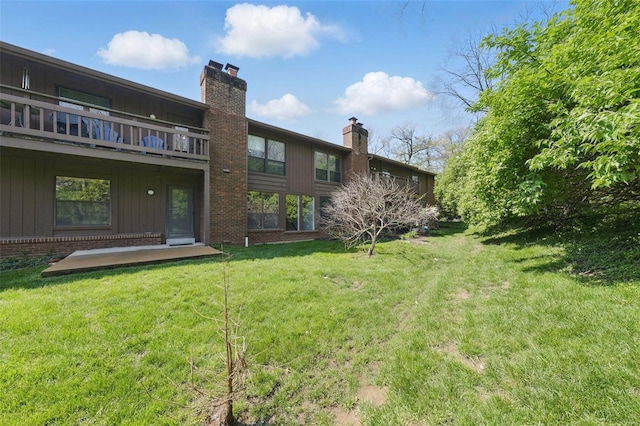back of property featuring a chimney, brick siding, a yard, and a balcony