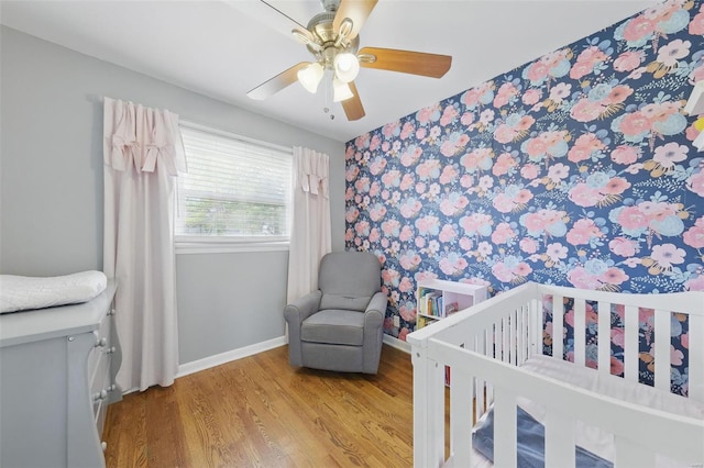 bedroom with wood finished floors, wallpapered walls, baseboards, an accent wall, and a ceiling fan