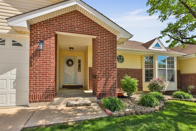 view of exterior entry with an attached garage, a shingled roof, and brick siding