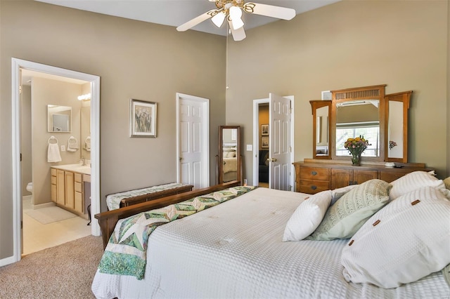 bedroom with a ceiling fan, ensuite bathroom, a sink, light carpet, and a towering ceiling