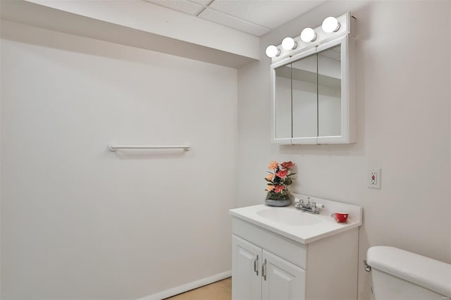 half bathroom featuring a paneled ceiling, toilet, and vanity