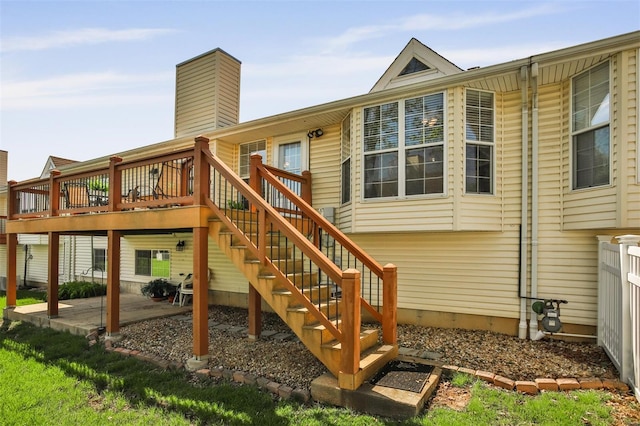rear view of house featuring a chimney, a wooden deck, stairs, and a patio