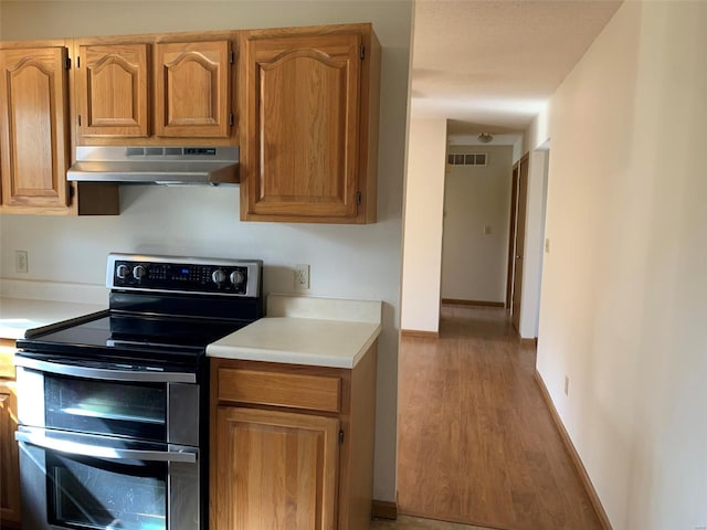 kitchen featuring light countertops, under cabinet range hood, visible vents, range with two ovens, and wood finished floors