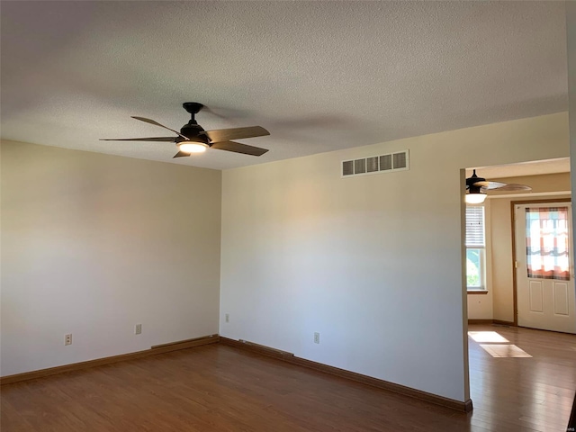 spare room with ceiling fan, a textured ceiling, visible vents, wood finished floors, and baseboards