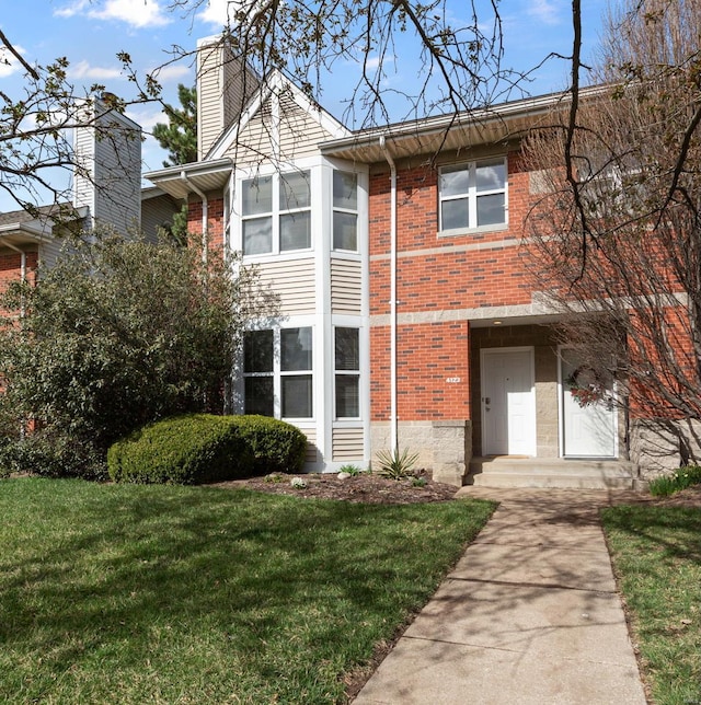 view of front of house with brick siding, a chimney, and a front yard