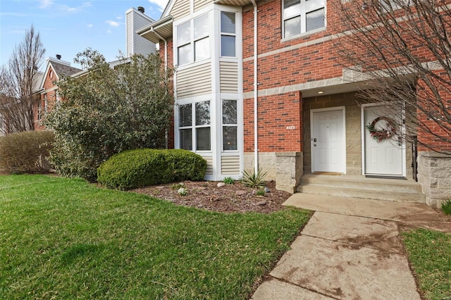entrance to property featuring a lawn and brick siding