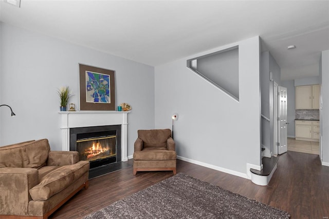 living area featuring baseboards, a fireplace with flush hearth, and wood finished floors