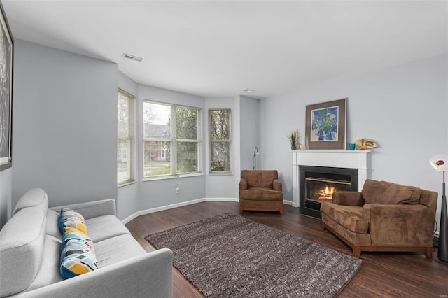 living area featuring a fireplace with flush hearth, baseboards, dark wood-type flooring, and visible vents