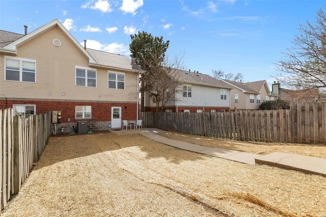 back of property featuring a fenced backyard, a residential view, central AC, and brick siding