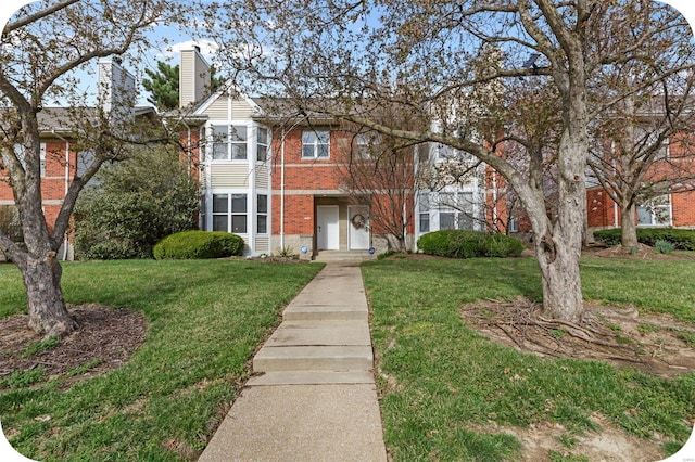 view of front of property featuring brick siding, a front lawn, and a chimney