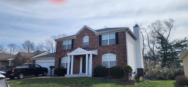colonial home with a front yard, a garage, a chimney, cooling unit, and brick siding