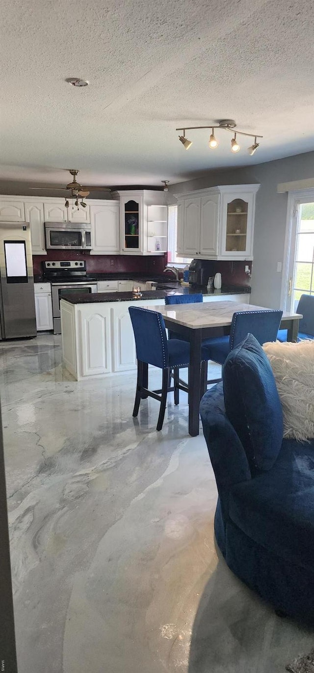 interior space with glass insert cabinets, a textured ceiling, white cabinets, appliances with stainless steel finishes, and dark countertops