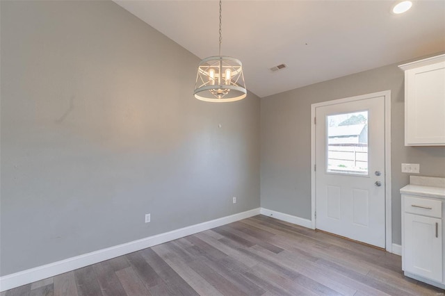 unfurnished dining area featuring baseboards, light wood-style flooring, visible vents, and a notable chandelier