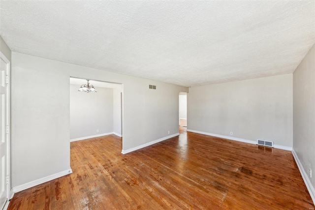unfurnished room featuring baseboards, visible vents, an inviting chandelier, and wood-type flooring