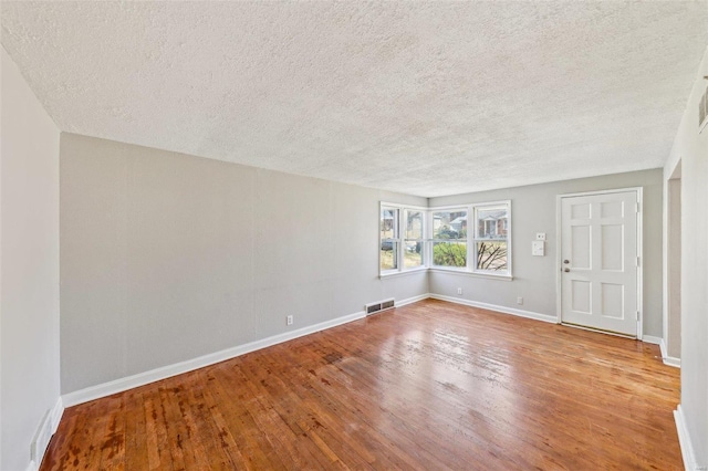 interior space featuring hardwood / wood-style flooring, baseboards, a textured ceiling, and visible vents