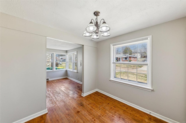 unfurnished dining area featuring wood finished floors, a notable chandelier, baseboards, and a wealth of natural light