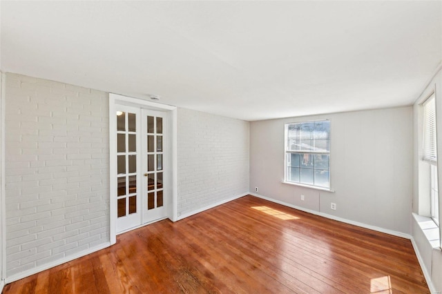 unfurnished room featuring baseboards, brick wall, and wood-type flooring