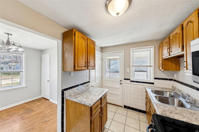 kitchen featuring light countertops, a sink, brown cabinetry, stove, and tile walls