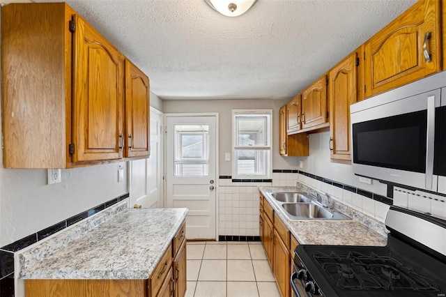 kitchen featuring light countertops, stainless steel gas range, brown cabinets, a sink, and light tile patterned floors