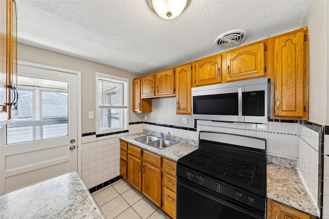 kitchen with light countertops, light tile patterned floors, a sink, visible vents, and black range with gas stovetop