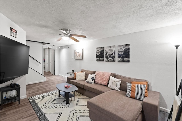 living room featuring a textured ceiling, baseboards, stairs, ceiling fan, and wood finished floors