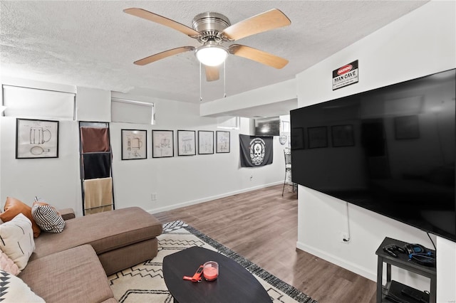 living room featuring baseboards, a textured ceiling, wood finished floors, and ceiling fan