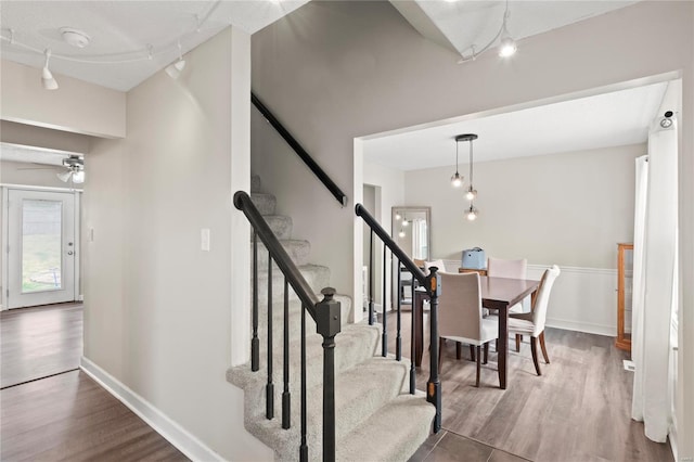 staircase with baseboards, wood finished floors, track lighting, and a ceiling fan
