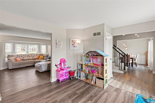 game room with wood finished floors, a textured ceiling, baseboards, and visible vents