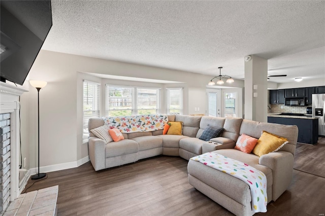 living area with a brick fireplace, a textured ceiling, baseboards, and wood finished floors