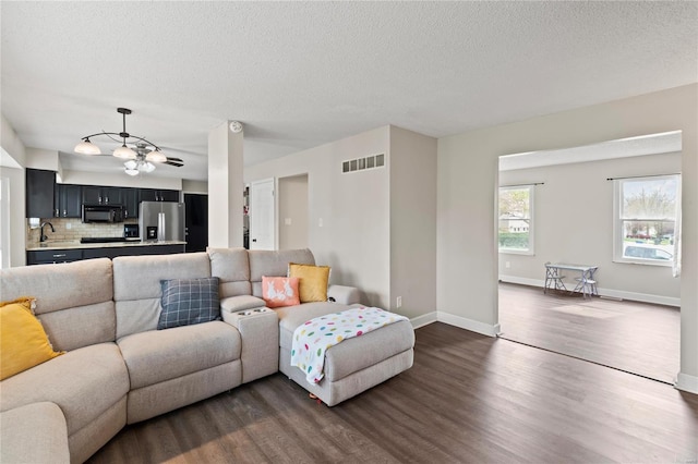 living room with dark wood-type flooring, baseboards, a textured ceiling, and visible vents