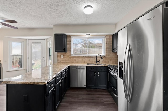 kitchen with stainless steel appliances, dark wood finished floors, a sink, a ceiling fan, and a peninsula