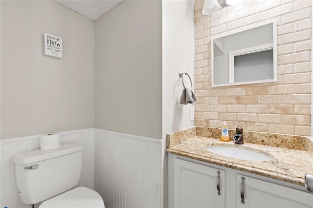 bathroom featuring a wainscoted wall, toilet, vanity, and a textured ceiling