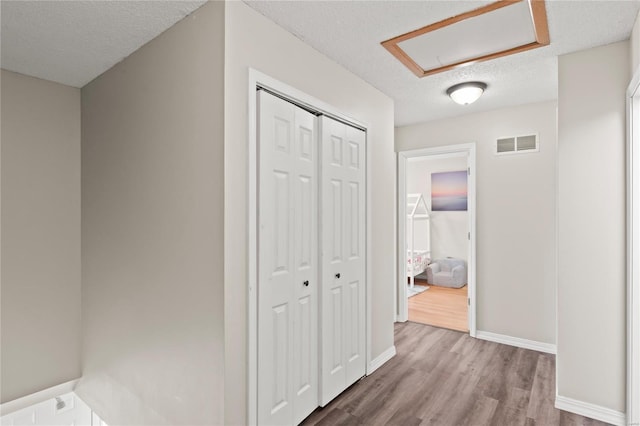 hall featuring baseboards, a textured ceiling, visible vents, and wood finished floors