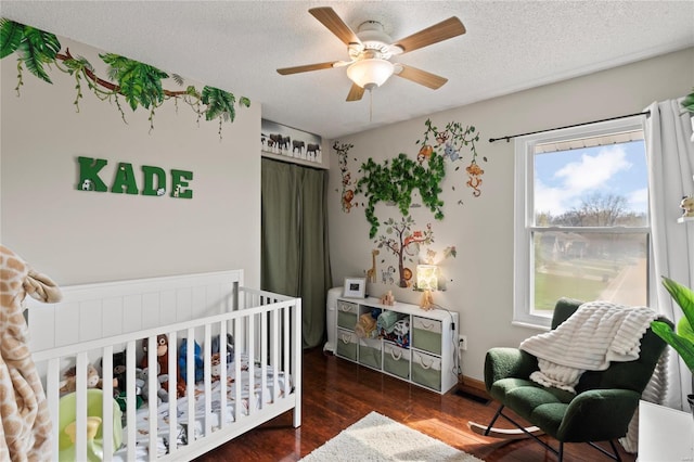 bedroom with a textured ceiling, baseboards, wood finished floors, a ceiling fan, and a nursery area