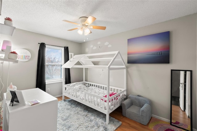 bedroom with baseboards, wood finished floors, ceiling fan, and a textured ceiling